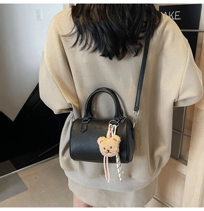 Detailed back view of a black lychee leather cylinder bag with a plush bear charm