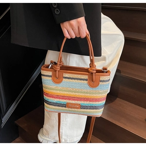 Dettaglio di borsa in paglia intrecciata a righe colorate con manici in pelle marrone