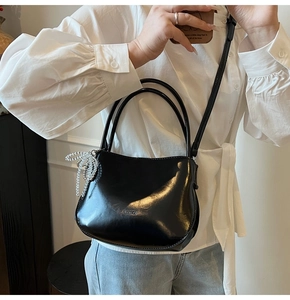 Détail du sac seau noir en cuir verni avec breloque nœud argenté et logo de marque
