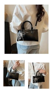 Close-up of black leather tote bag featuring a silver metal bow and white lettering
