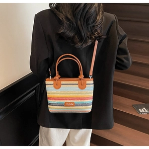 Dettaglio borsa in paglia a righe colorate con manici in pelle marrone e logo