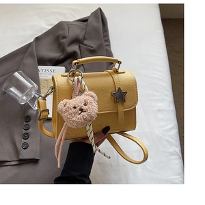 Detail of yellow lychee textured leather mini bag with metal star buckle and teddy bear charm