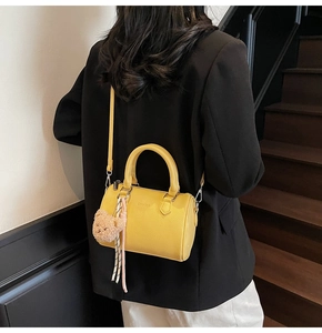 Detail of yellow pebbled leather barrel bag with dual handles and cute brown bear charm