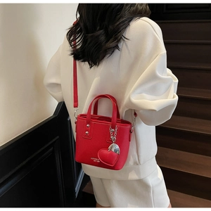 Detail of red bucket bag with litchi texture leather, silver hardware and heart charm