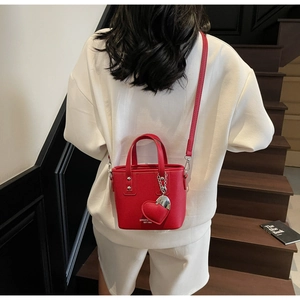 Detail of red pebbled leather bucket bag with heart charm shown in a crossbody style