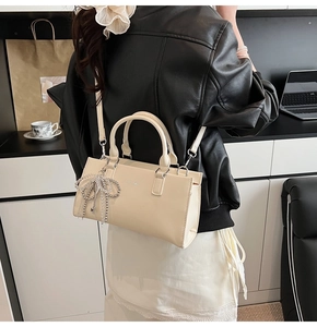 Detail view of a beige matte leather tote bag with elegant metallic charm on model