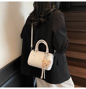 Detailed view of a white leather cylinder bag with handles and a brown plush bear charm