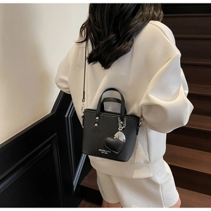 Detail of a black lychee leather bucket bag with heart charm worn by a model on stairs