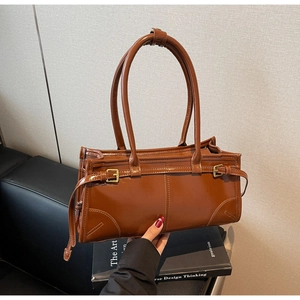 Detail of brown patent leather shoulder bag with decorative buckle straps and glossy finish