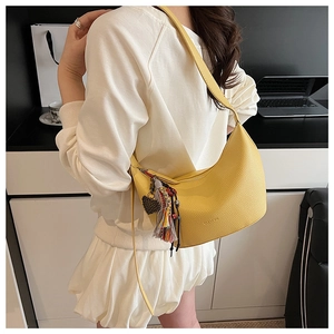 Détail du sac demi-lune jaune avec texture litchi et pendentif à pompon bohème