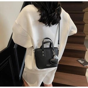 Detail of black lychee leather bucket bag with silver heart charm on model