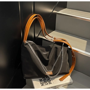 Detail of black canvas tote bag featuring brown leather handles and silver chain accents