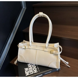Minimalist cream shoulder bag with thin straps and gold buckles on architectural book