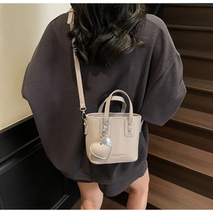 Detail view of beige bucket bag with silver heart charm and textured pebbled leather finish