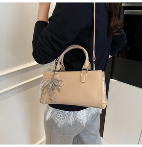 Detail of light khaki leather tote bag with silver logo and beaded bow key pendant