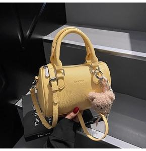 Detail of yellow boston bag with pebble leather texture, silver hardware and bear charm