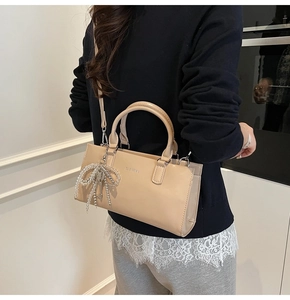 Detail of beige rectangular handbag with silver lettering and beaded bow charm