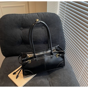 Detail of a minimalist black leather underarm bag with gold hardware on a vintage chair