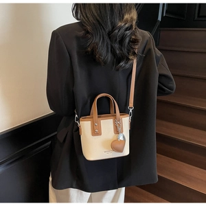 Detail of a chic cream bucket bag with brown trim shown on a model by a staircase