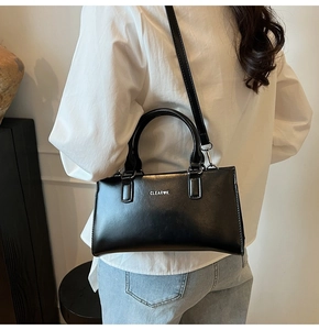 Close-up of CLEAR K logo on a black leather tote bag worn by a model in a room