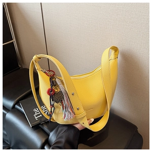 Détail du sac hobo en cuir grainé jaune avec des pompons colorés de style ethnique