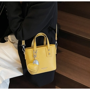Detail of a bright yellow bucket bag with litchi texture and a heart charm on stairs