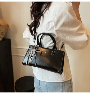 Detail of black glossy shoulder bag with silver bow charm and elegant leather texture