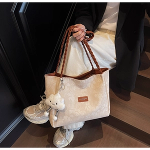 Detail of floral embossed tote bag with dark braided handles and white cloud charm