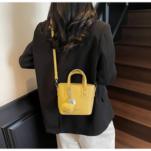 Detail of a bright yellow bucket bag featuring lychee texture and heart charm pendant
