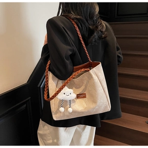 Detail of off-white tote bag with woven brown leather straps and cloud plush charm