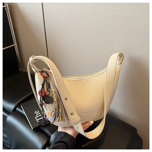 Détail du sac demi-lune beige en cuir grainé avec un pendentif à pompon coloré