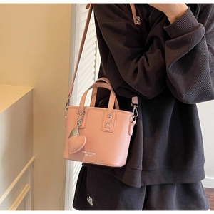Detail of pink lychee leather mini bucket bag with heart charm and metal chain strap
