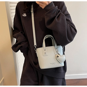 Detail of mint green bucket bag with heart charm and silver chain on model