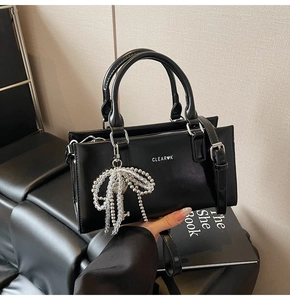 Close-up of black crossbody tote bag featuring white bead bow charm and silver hardware