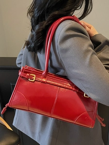 Glossy bright red rectangle underarm bag with gold buckles on a dark suit background