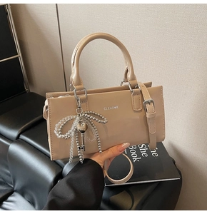 Detail of beige leather tote bag with a silver pearl bow charm and key pendant