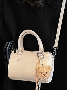 Chic beige cylinder Boston bag in lychee pattern leather with a cute plush bear charm