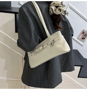 Close-up of a cream leather underarm bag featuring a buckle strap and heart-shaped charm
