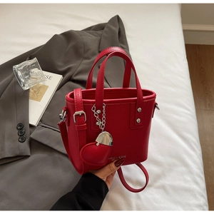 Detail of red pebbled leather mini bucket bag with heart charm and silver chain