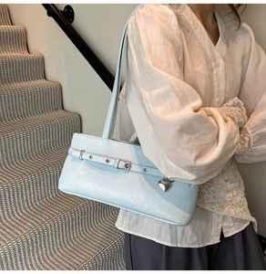 Detail view of light blue leather underarm bag featuring a metallic heart-shaped pendant