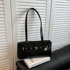 Close-up of black patent leather underarm bag with silver heart charm and belt buckle