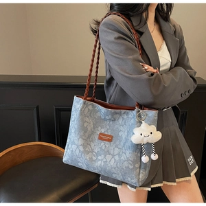 Detail of blue floral tote bag with brown woven straps and white cloud plush charm