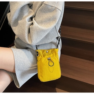 Close-up of yellow nylon mini crossbody bag with drawstring pocket on grey sweater