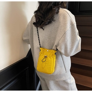 Detail view of mini yellow nylon crossbody bag with drawstring closure on person