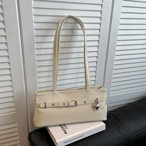 Detail of off-white shoulder bag featuring silver heart charm and metal eyelet strap
