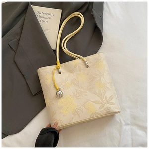 Close-up of floral tote bag with silver bell charm and yellow slim shoulder strap