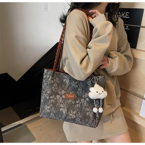Detail of grey floral tote bag with brown woven strap and white plush cloud charm accessory
