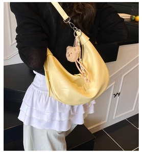 Detail of pale yellow crescent bag with crocodile pattern and plush bear charm on model