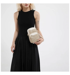 Detail of woven straw mini crossbody bag with double zippers and leather trim on a model