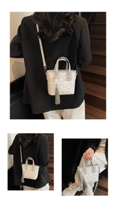 Detail showing the cream embroidered crossbody bucket bag with grey tassel and silver hardware